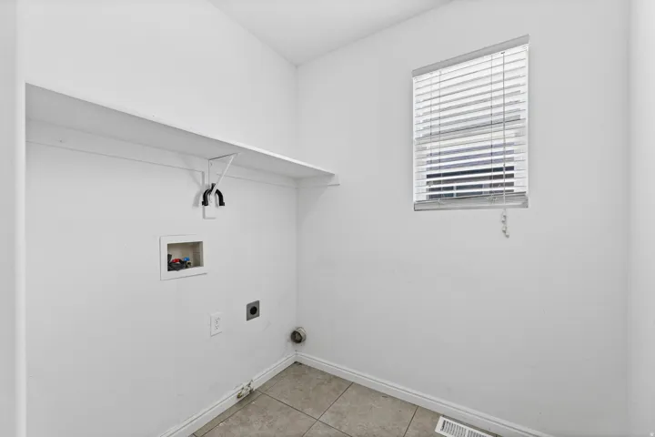 Second laundry room with utility hookups, upper shelf storage, and a window providing natural light.