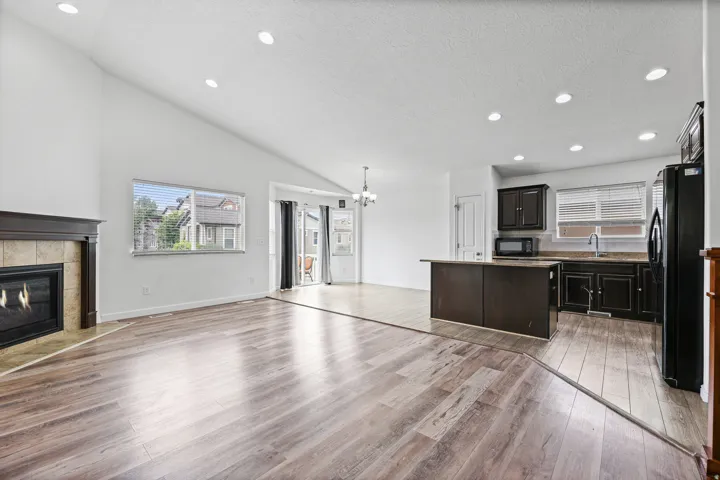 Bright living room with vaulted ceilings, large windows, and a gas fireplace that serves as a welcoming focal point. Sliding glass doors provide easy access to the backyard.