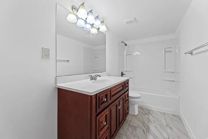Full bathroom featuring a vanity with storage, a large mirror, and a tub/shower combination in a clean, functional design.