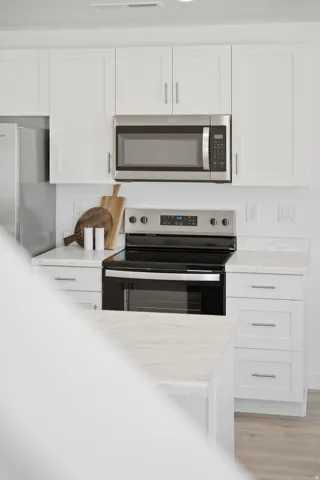 Modern kitchen featuring white shaker cabinetry, stainless steel appliances including a microwave and range, and light-toned countertops