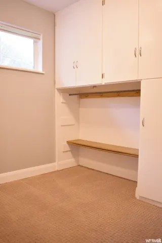 Built-in white cabinetry with chrome hardware, integrated bench seating, wood-finish coat rack, and textured carpeting