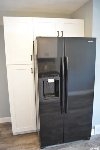 Built-in black side-by-side refrigerator with exterior ice and water dispenser, complemented by white shaker-style cabinetry with dark hardware, wood-finish flooring, and light gray walls