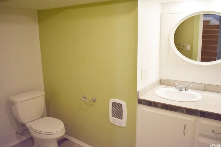 Bathroom featuring a white toilet, light green accent wall, white vanity with integrated sink, stone-look countertop, and an oval mirror