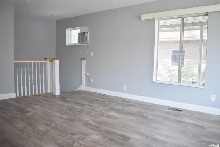 Spacious room featuring wood-finish flooring, light grey walls, white baseboards, and a large window with horizontal blinds