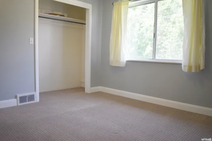 Carpeted room featuring a window with an exterior tree view, a built-in closet with shelving, light gray wall paint, and white baseboards