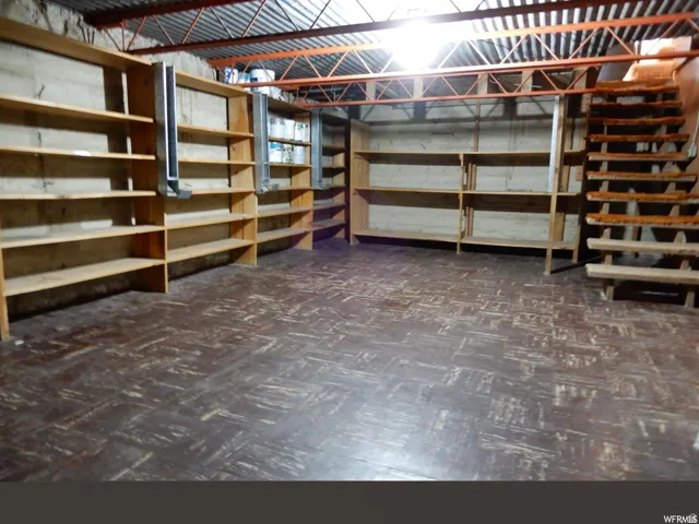 Spacious storage area featuring extensive built-in wooden shelving, exposed ceiling joists, and a partial wooden staircase
