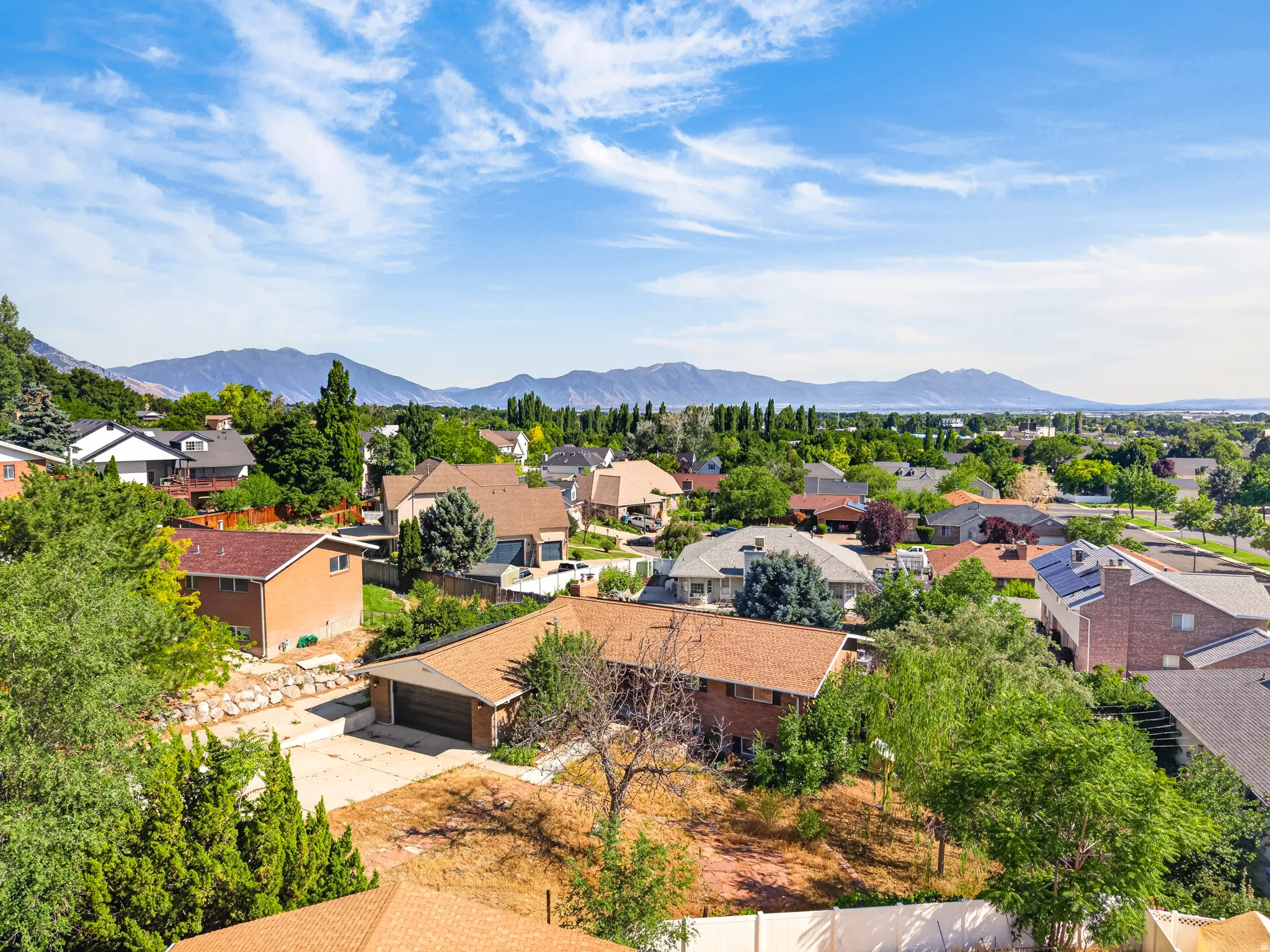 Residential neighborhood with diverse home styles, mature landscaping, and mountain backdrops
