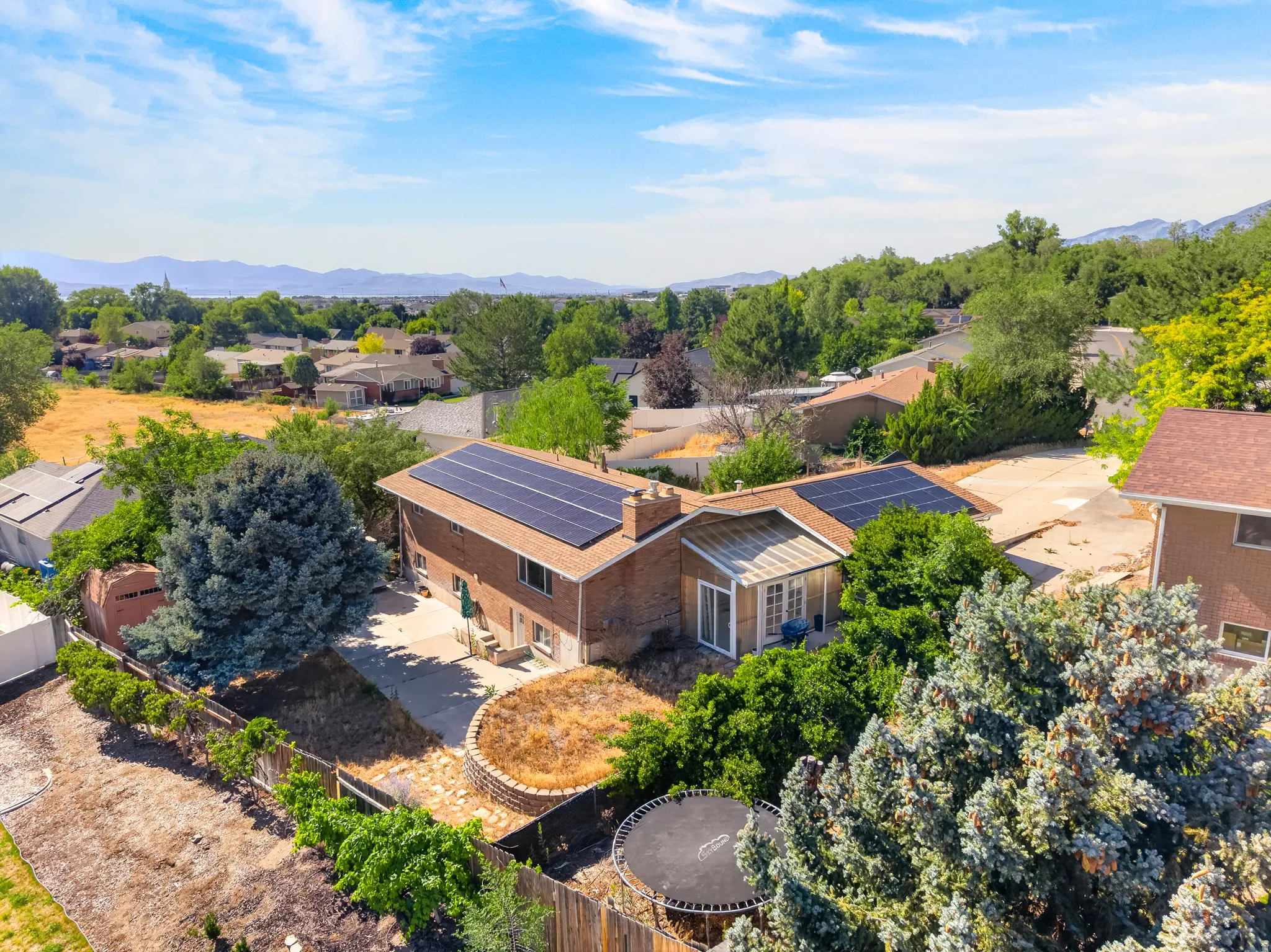 Brick exterior residential property with solar panels, a paved patio, and mature landscaping
