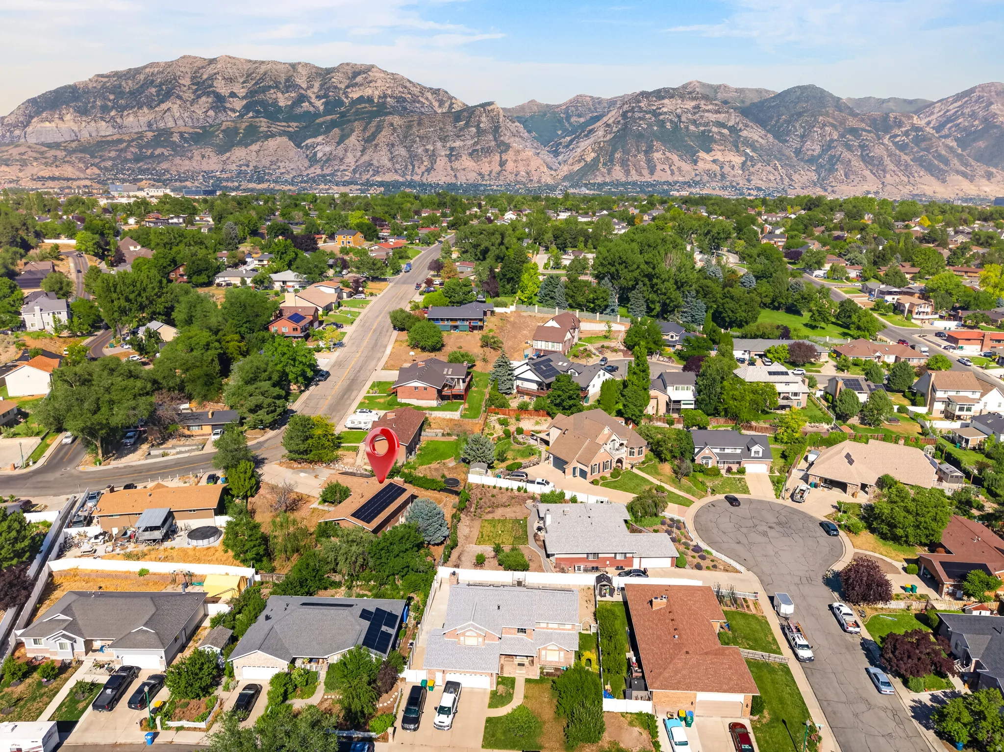 Residential neighborhood with varied architectural styles and abundant mature trees, situated against a dramatic mountain range backdrop