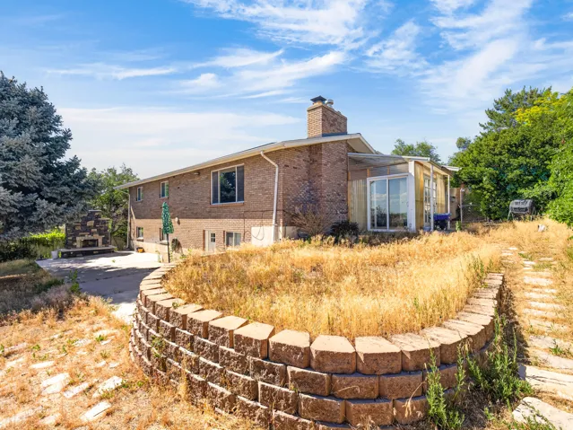 Brick exterior residence featuring a stone-clad outdoor fireplace, sliding patio doors, a retaining wall, and mature perimeter trees
