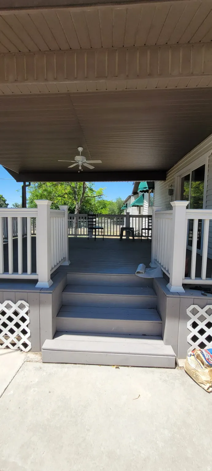 Covered deck with a ceiling fan, white railings, and steps leading to a concrete patio