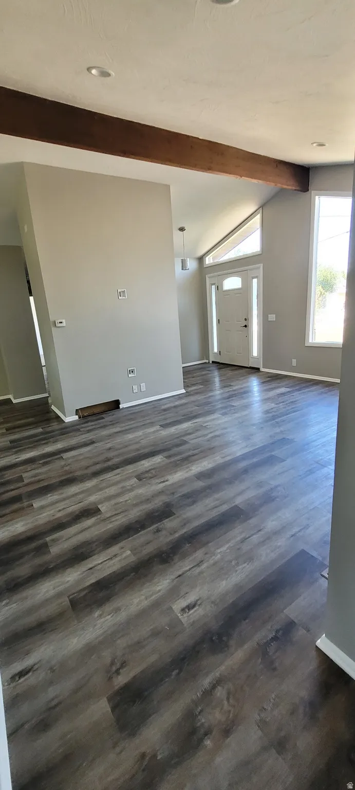 Spacious interior featuring wood-finish flooring, vaulted ceilings, exposed beam accents, recessed lighting, and a front entry door with a transom window