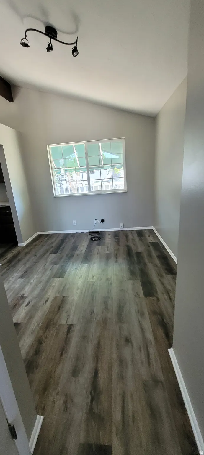 Spacious room featuring wood-finish flooring, light grey walls, white baseboards, and a vaulted ceiling with track lighting