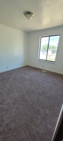 Room featuring wall-to-wall carpeting, white painted walls, and a large window with a black frame