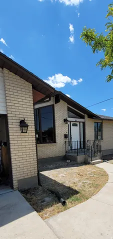 Light brick exterior featuring a prominent bay window, white entry door with a black security screen, and a concrete pathway