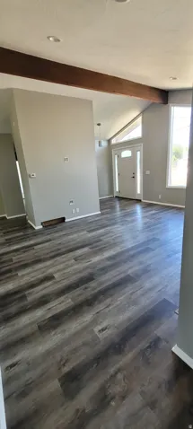 Spacious interior featuring wood-finish flooring, vaulted ceilings, exposed beam accents, recessed lighting, and a front entry door with a transom window