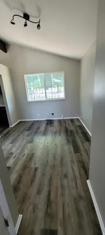 Spacious room featuring wood-finish flooring, light grey walls, white baseboards, and a vaulted ceiling with track lighting