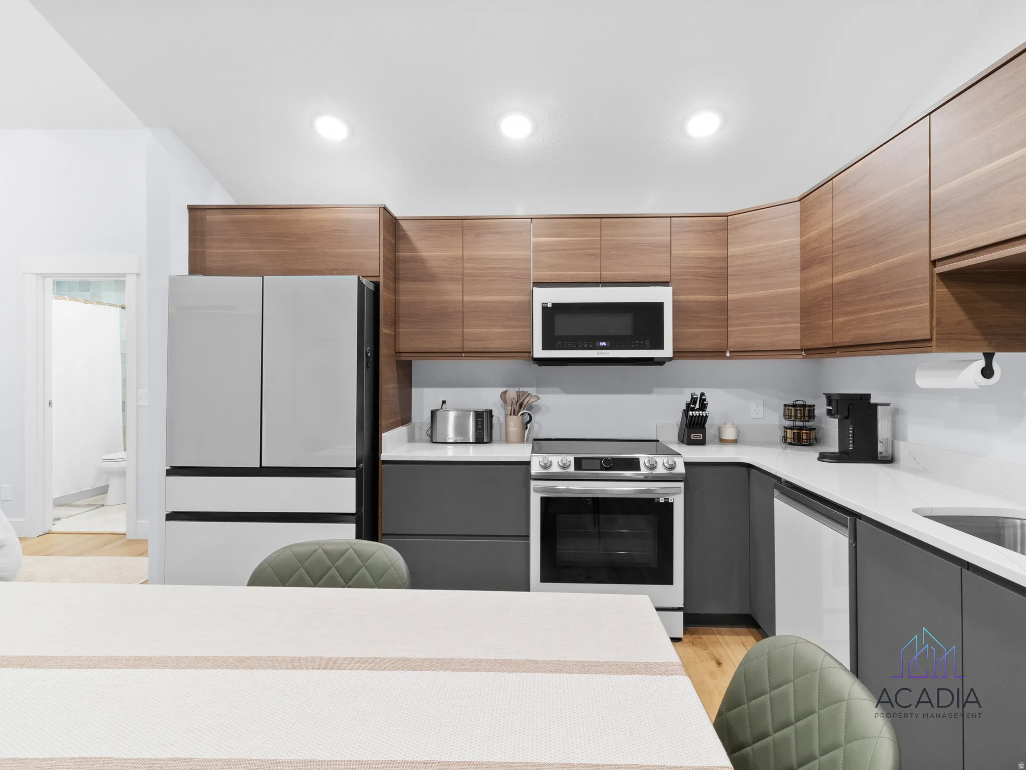 Contemporary kitchen featuring wood-finish upper cabinetry, gray lower cabinetry, white countertops, and stainless steel appliances