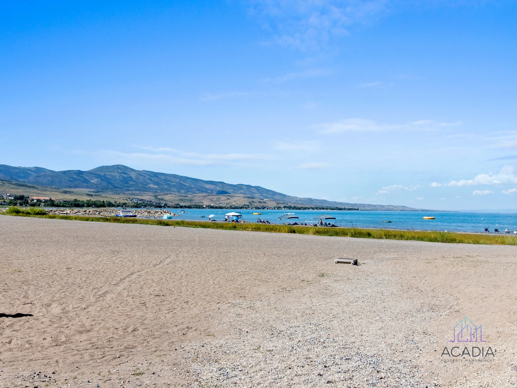 Expansive sandy beach with deep blue water, distant mountains, and a clear sky
