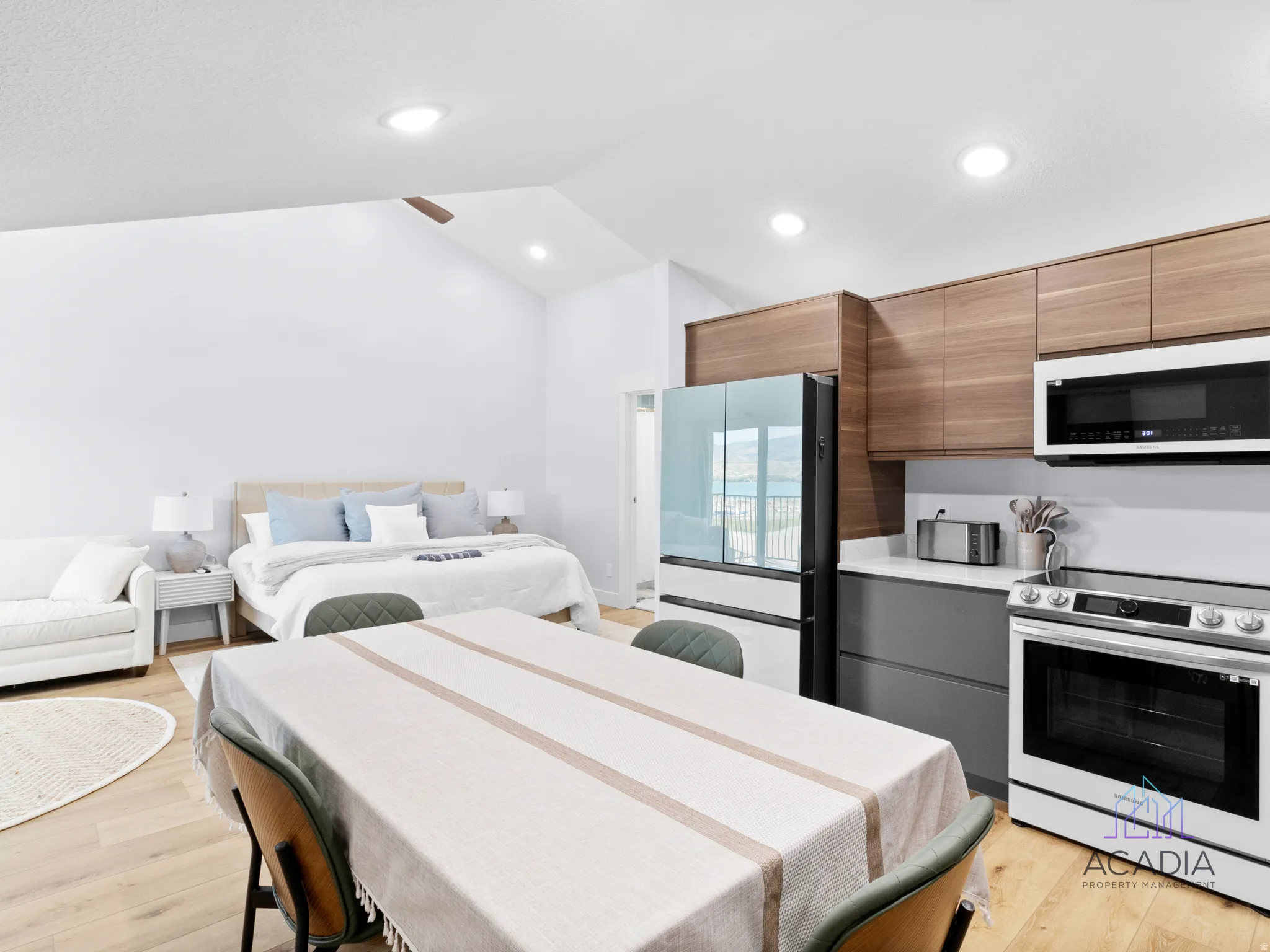 Open-concept studio space featuring vaulted ceilings, wood-finish flooring, a modern kitchen with integrated appliances, wood-tone upper cabinetry, and recessed lighting