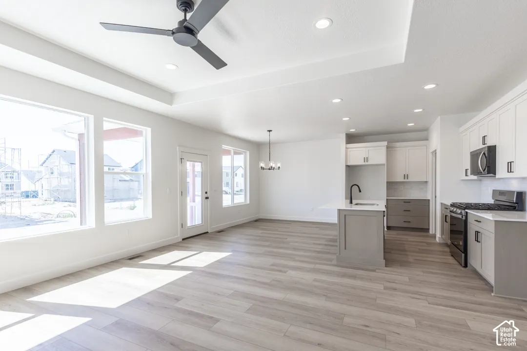 Open-concept living space featuring wood-finish flooring, recessed lighting, and a tray ceiling with a ceiling fan