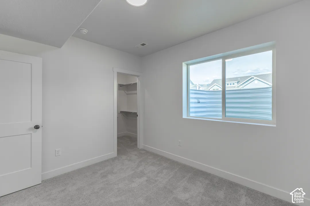 Room featuring light gray carpeting, crisp white walls, a single window with a privacy blind, and an open closet with built-in shelving