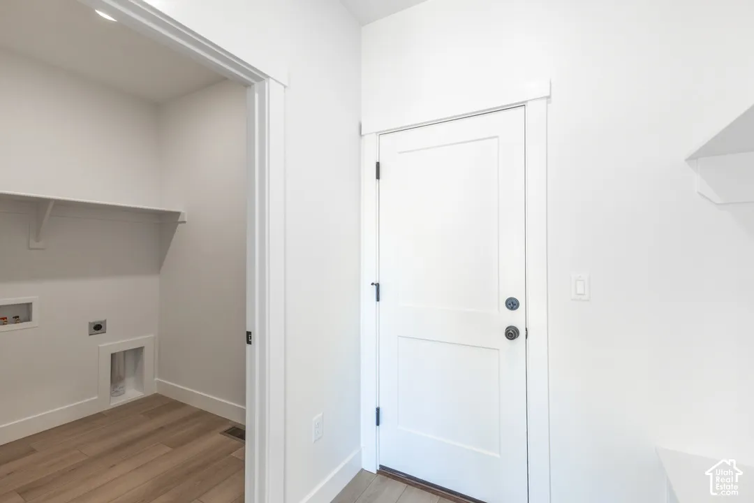 Dedicated laundry area featuring a built-in shelf, appliance hookups, wood-finish flooring, and crisp white trim