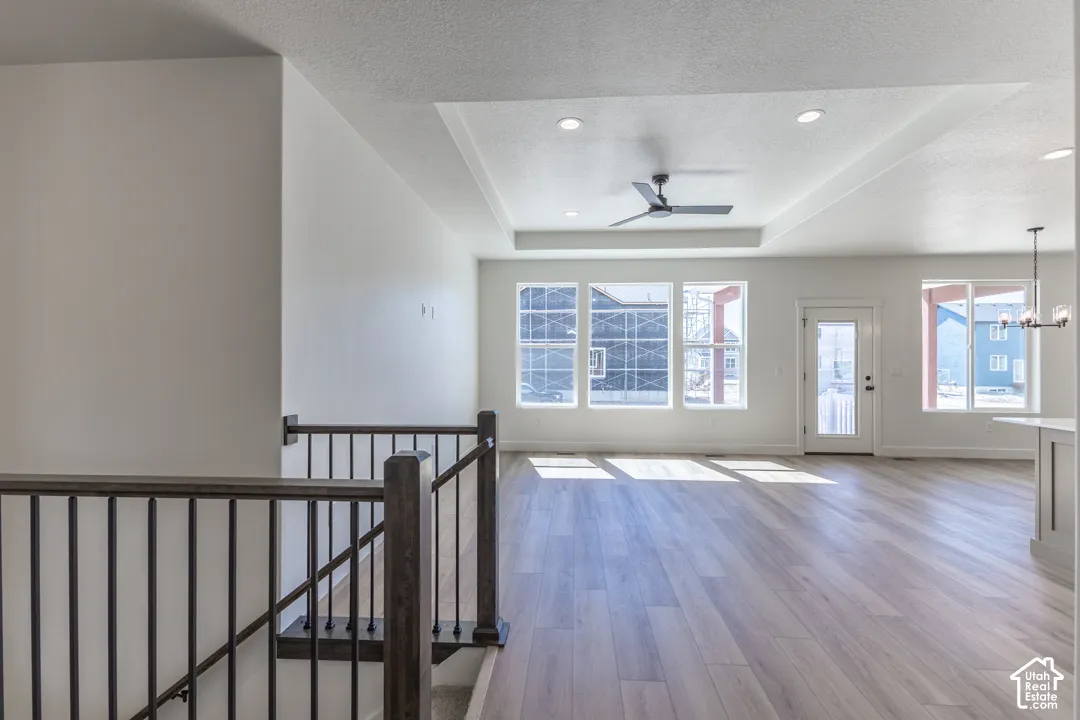 Spacious open-concept living area featuring wood-finish flooring, a tray ceiling with recessed lighting, and a modern ceiling fan