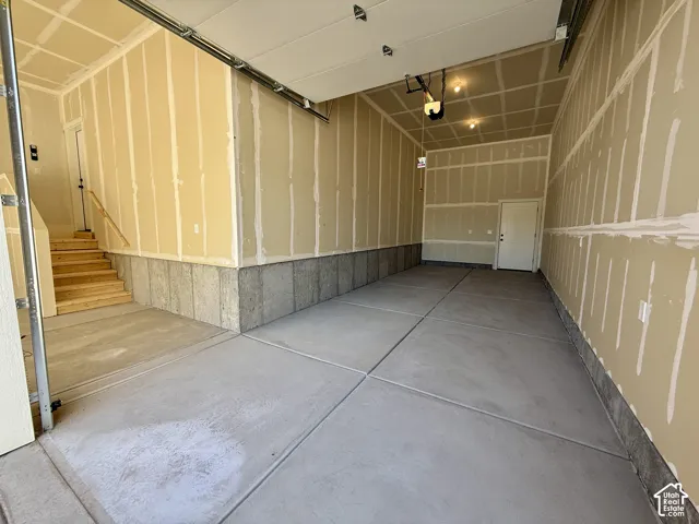 Multi-car garage featuring concrete flooring, concrete foundation walls, finished drywall, and interior access via a wooden staircase