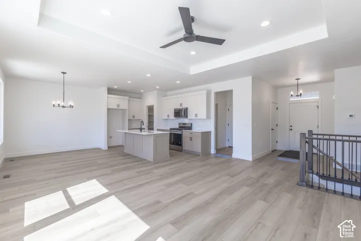 Open-concept living space featuring wood-finish flooring, a tray ceiling with recessed lighting and a ceiling fan, and a kitchen island with a sink and modern faucet