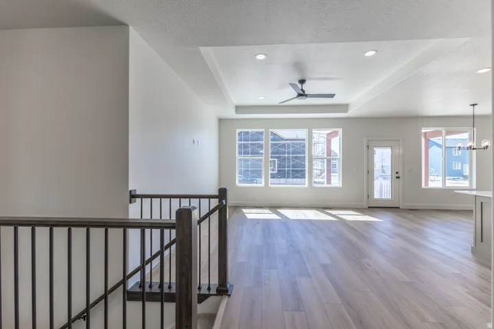 Spacious open-concept living area featuring wood-finish flooring, a tray ceiling with recessed lighting, and a modern ceiling fan