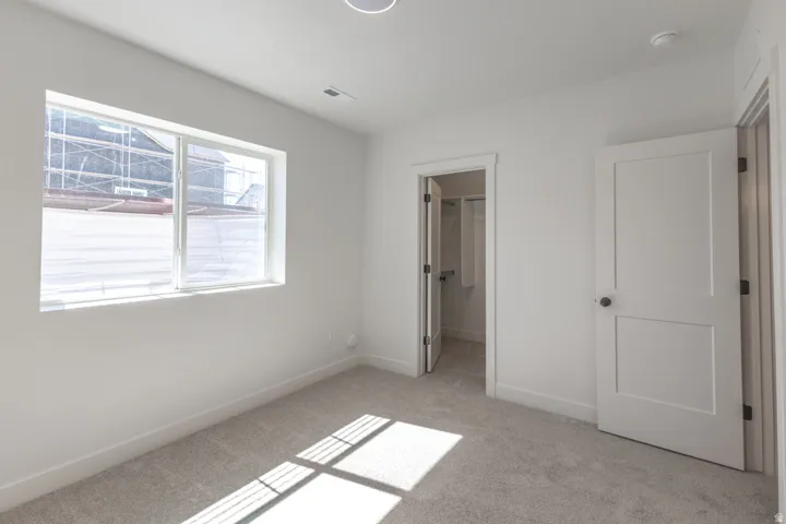 Carpeted room with a large window, a ceiling light fixture, a door with a black knob, and a separate closet with a bifold door