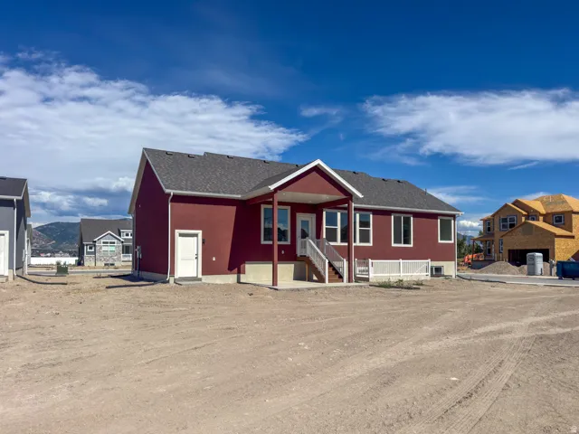 Newly constructed residence featuring a deep red exterior with white trim, a covered patio, and a walk-out basement entry