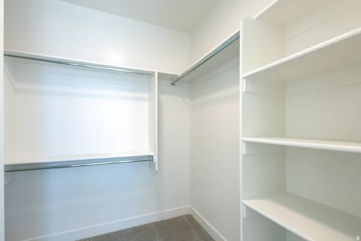 Walk-in closet featuring built-in shelving, dual hanging rods, and light-toned carpeting