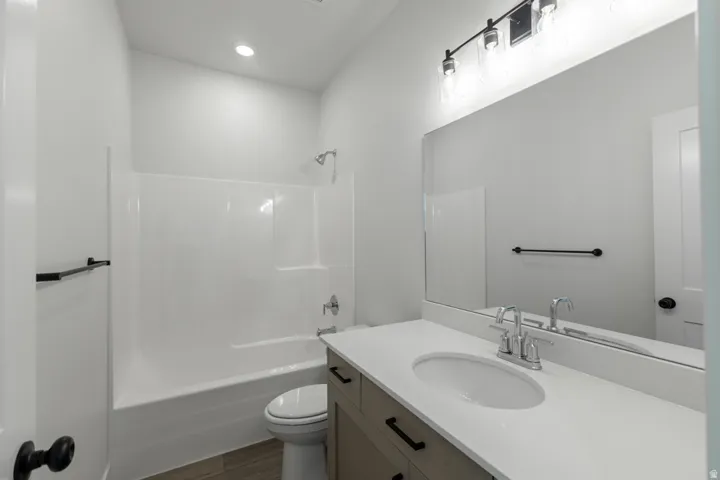 Bathroom featuring a light wood-finish vanity with a white countertop and undermount sink, a large wall-mounted mirror, and a white tub/shower combination