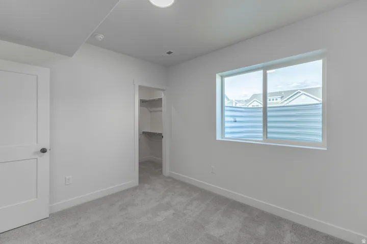 Room featuring light gray carpeting, crisp white walls, a single window with a privacy blind, and an open closet with built-in shelving