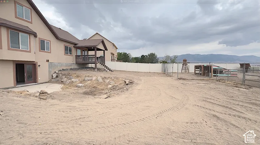 Expansive undeveloped backyard with mountain scenery, featuring a covered deck, lower-level patio, and chain-link fencing