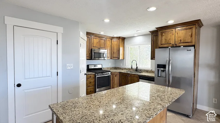 Kitchen featuring a central island with a granite-style countertop, stainless steel appliances, wood-finish cabinetry, and recessed lighting