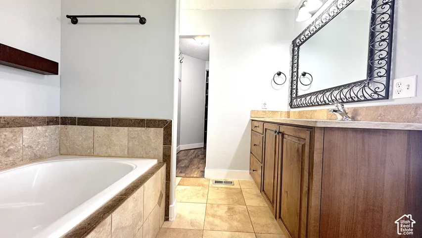 Primary bathroom featuring a built-in tub with tile surround, wood-finish vanity with countertop, and a decorative framed mirror.