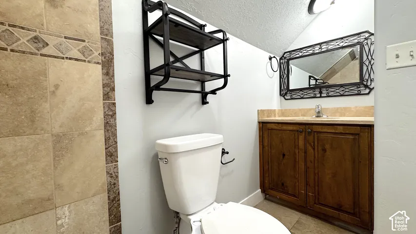 Upstairs hallway bathroom featuring a wood-finish vanity with a granite  countertop, a decorative framed mirror, and tile flooring.