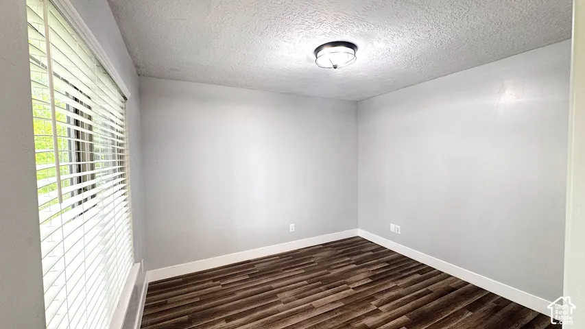 Front of house office, bright interior room featuring a large window with white blinds, wood-finish flooring, light gray wall paint, white baseboards, and a flush-mount ceiling light fixture