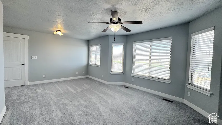 Spacious Primary Bedroom featuring light gray walls, plush gray patterned carpeting, and a ceiling fan, with brand new carpet.