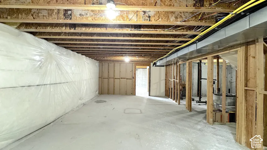 Unfinished basement space featuring a concrete floor, exposed wood framing, ceiling joists, and a partial insulated wall