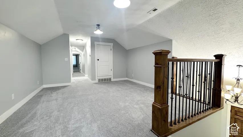 Carpeted open loft area featuring a wood newel post and baluster railing, sloped ceilings, recessed lighting, and a paneled storage door