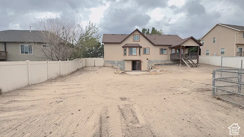 Expansive backyard featuring a covered patio, a walk-out basement entry, a wooden deck with stairs, a bay window, and a tan vinyl fence