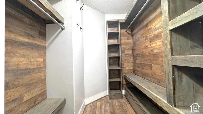 Primary custom closet system featuring wood-finish flooring, wood plank accent wall, built-in shelving, and hanging rods.