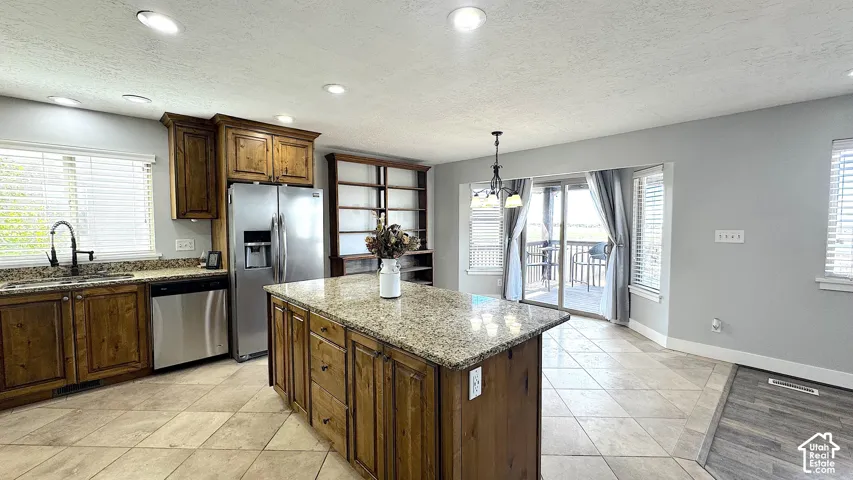 Spacious kitchen featuring a central island with a speckled countertop, coordinating perimeter countertops, rich wood cabinetry, stainless steel appliances, and tile flooring