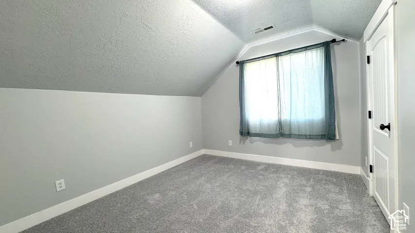Bedroom with new carpet, a paneled door with black hardware, neutral gray walls and white baseboards.