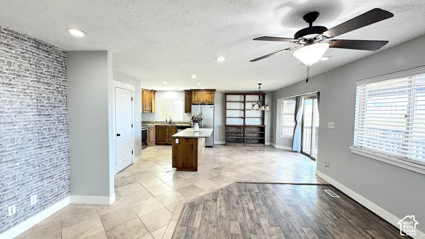 Spacious living area featuring a wood-finish flooring, a contemporary ceiling fan, and a large window with blinds