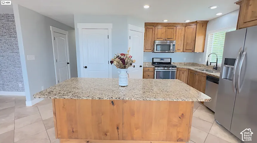 Kitchen featuring a large central island with granite countertop, wood cabinetry, stainless steel appliances, and tile flooring